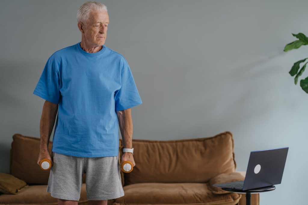 Free Senior man lifting dumbbells at home, staying fit with an online workout session. Stock Photo